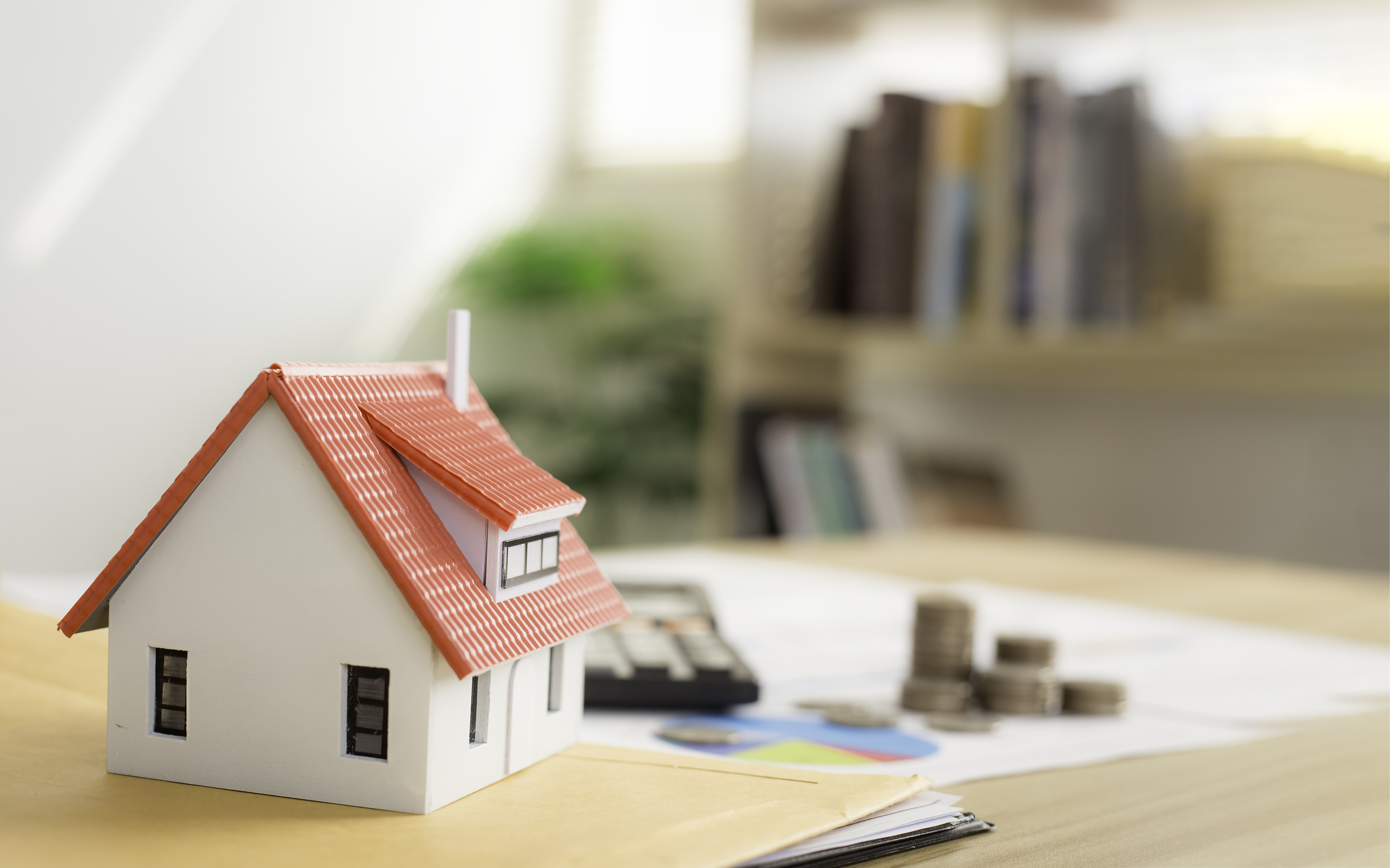 a house figurines and some coins on a desk